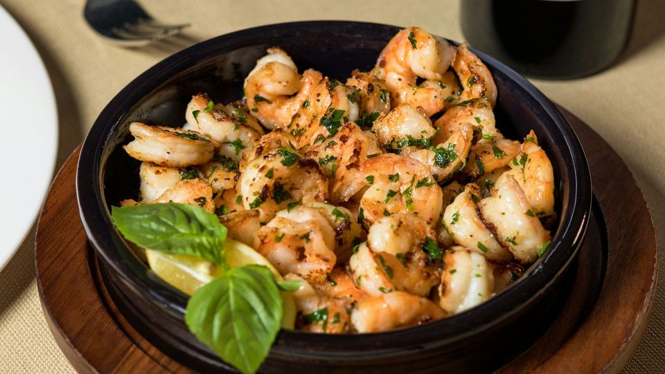 Bowl of grilled shrimp garnished with parsley, basil, and lemon wedges.