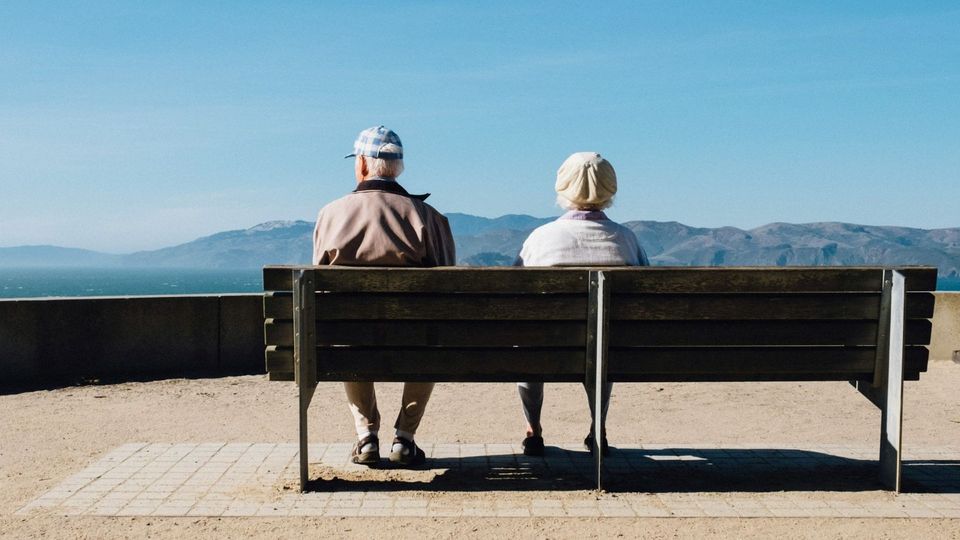 Older couple sitting on a bench overlooking the sea.