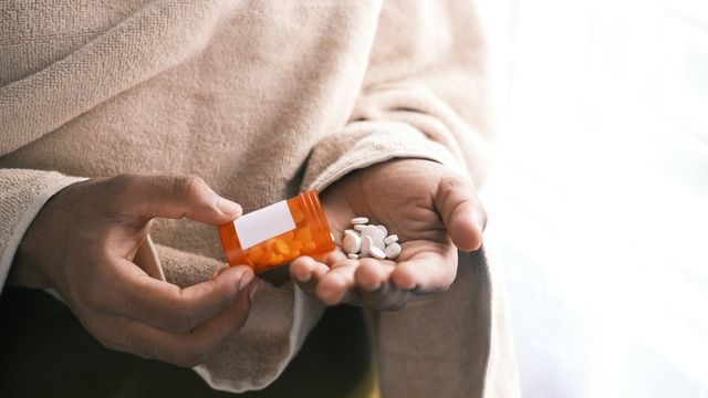 Mid-section of a person pouring white pills from an orange container into their hand. 