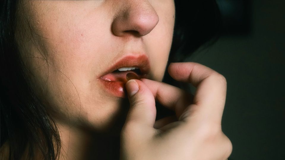 Woman placing an oral medication pill into her mouth, in a dark environment.