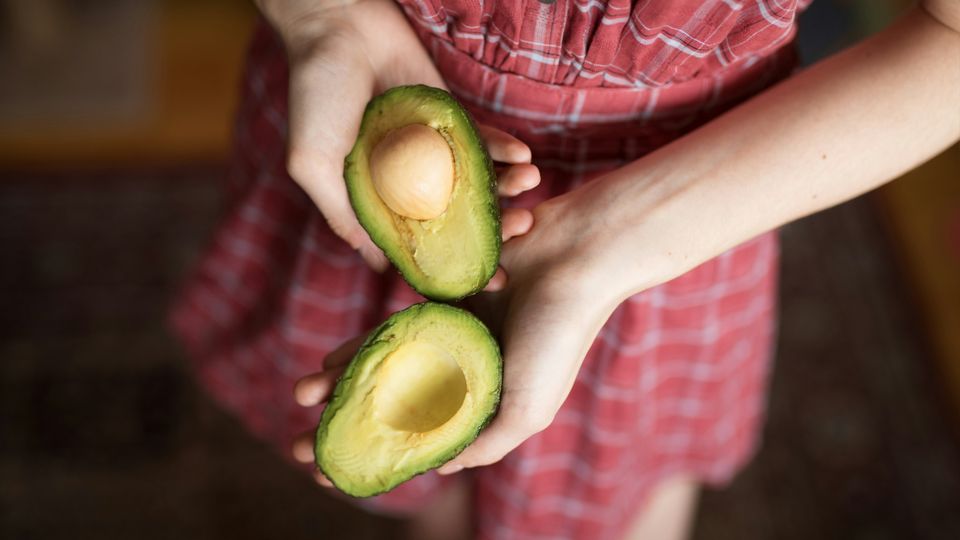 A woman holding two halves of an avocado.