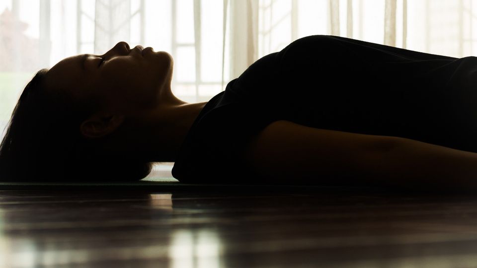 Person lying on a floor in profile beside sunlit windows, illustrating psychedelics-assisted therapy.