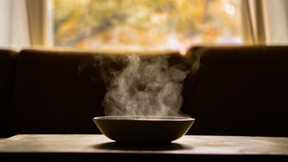 Bowl of steaming soup on a table.