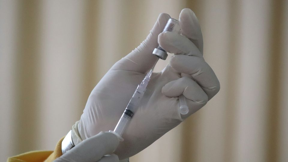 A clinician prepares a vaccine by inserting a needle into a vial.