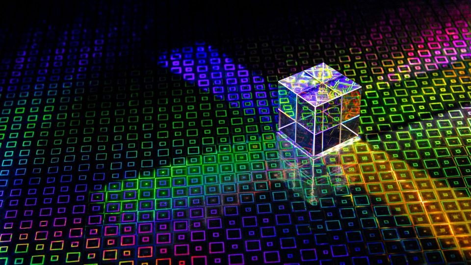 Glass prism cube reflecting rainbow light on a colorful geometric surface.