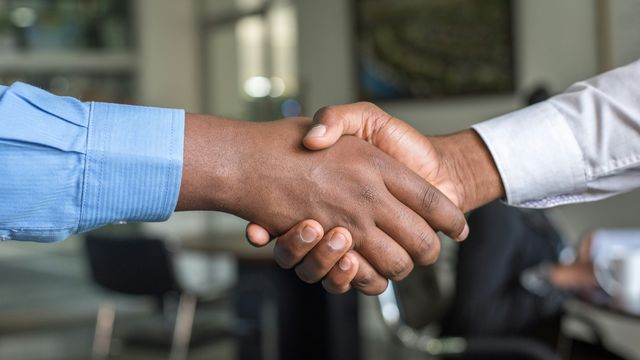 Close-up of two hands shaking, as if striking a deal, in an office settting. 
