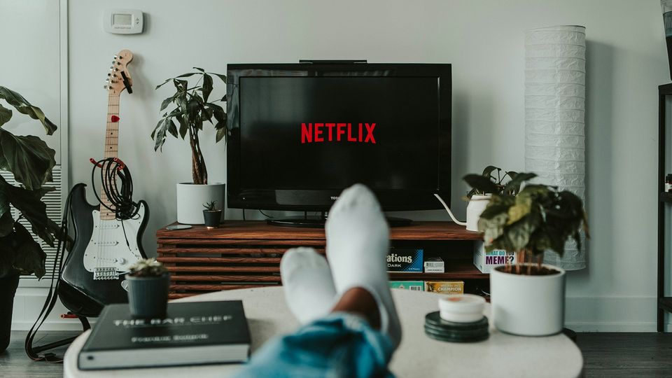 Person relaxing with feet up, watching TV displaying Netflix in a modern living room.