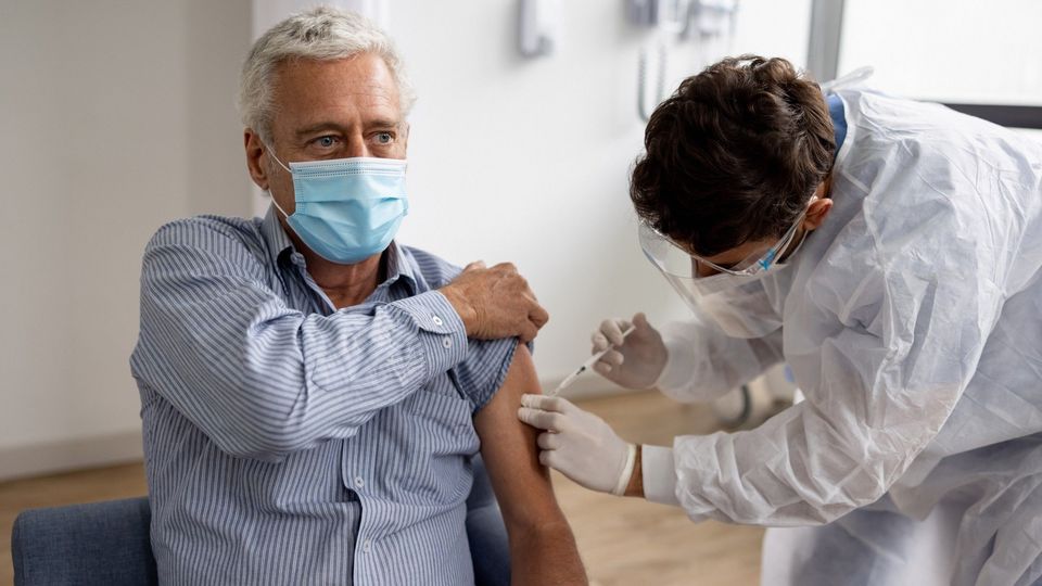 A healthcare worker, wearing a face mask, administering a vaccine into an elderly person's upper arm.
