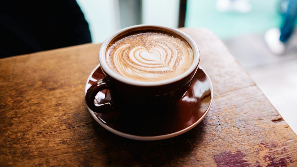 Cup of coffee with heart latte art on a wooden café table.