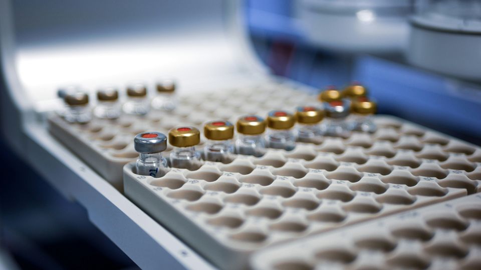 Vials with gold and silver tops placed into numbered slots within a rack, in a compound library facility.