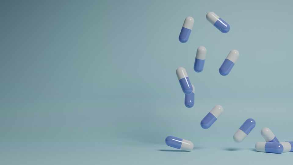 Blue and white capsules falling vertically to a flat surface against a light blue background.