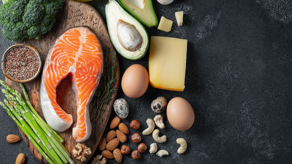 Flat-lay photography of key elements of the keto diet: oily fish, cheese, eggs, avocado, nuts, and seeds.