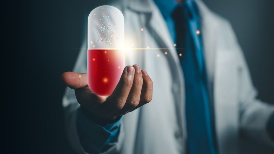 Doctor in a white coat holding an oversized red and white medicinal capsule. The capsule is glowing and contains a ball and stick model. 