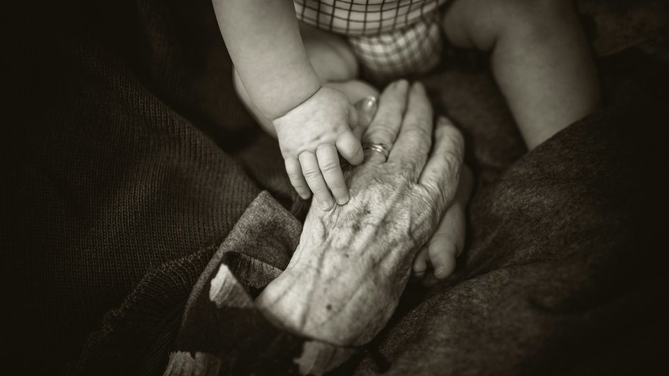 Birds-eye view of a baby holding an elderly person's hand in grey-scale.