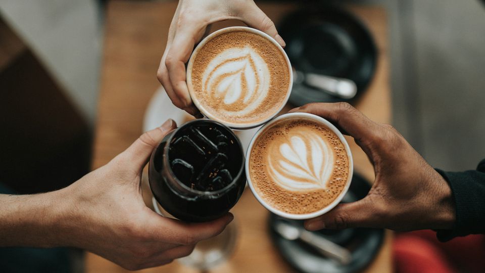 Three people holding up coffee cups containing different types of coffee drinks.