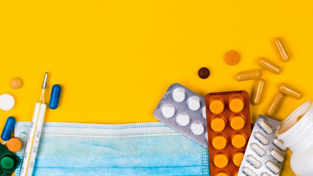 Medicine pills, a face mask, and an oral thermometer scattered on a tabletop. 