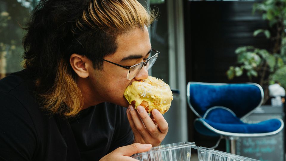 A young man sitting outside, eating a donut.