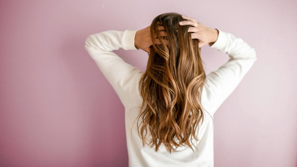 The back of a woman's head, as she puts her hands through long hair.