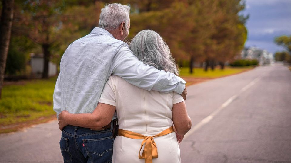Elderly couple walking arm in arm down a quiet road.