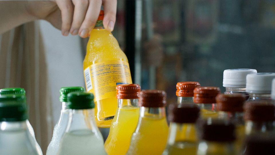 A person selecting a soda from rows of different sodas on a shelf.
