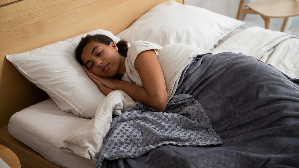 A woman sleeping in a bed underneath a weighted blanket.