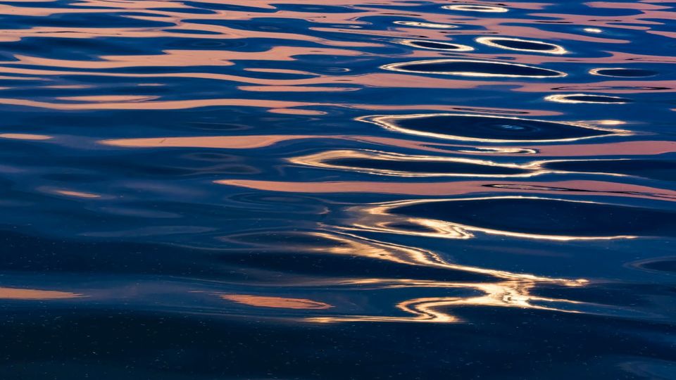 Rippling water reflecting blue and pink sunset light, creating abstract wave patterns.