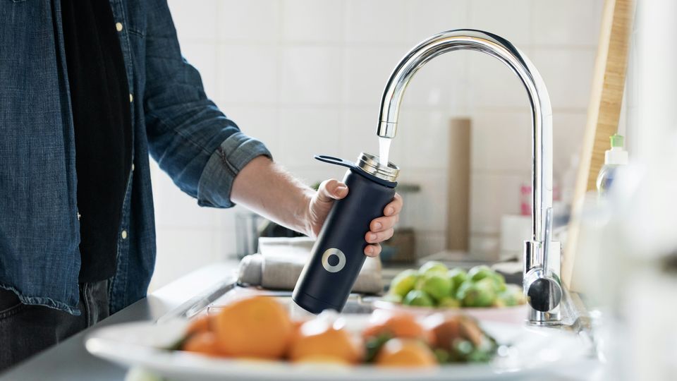 A person filling a metal water bottle from a kitchen tap.