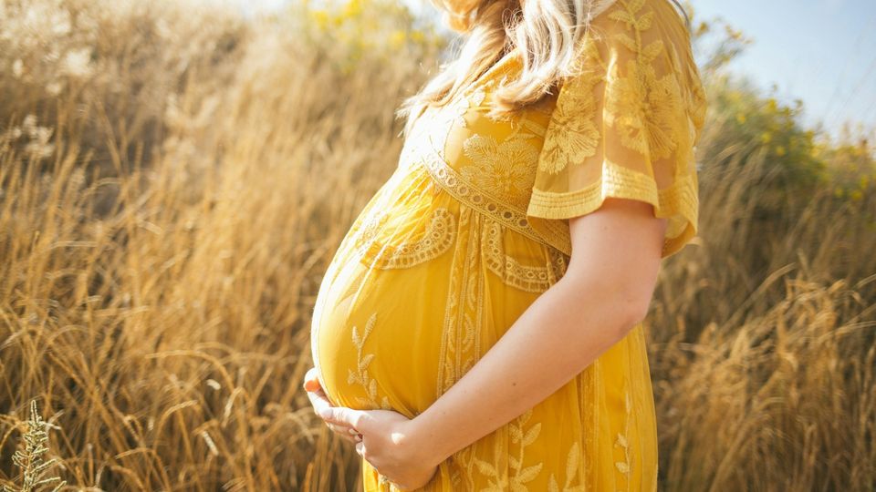 Pregnant woman wearing a yellow dress, holding her baby bump in a field.