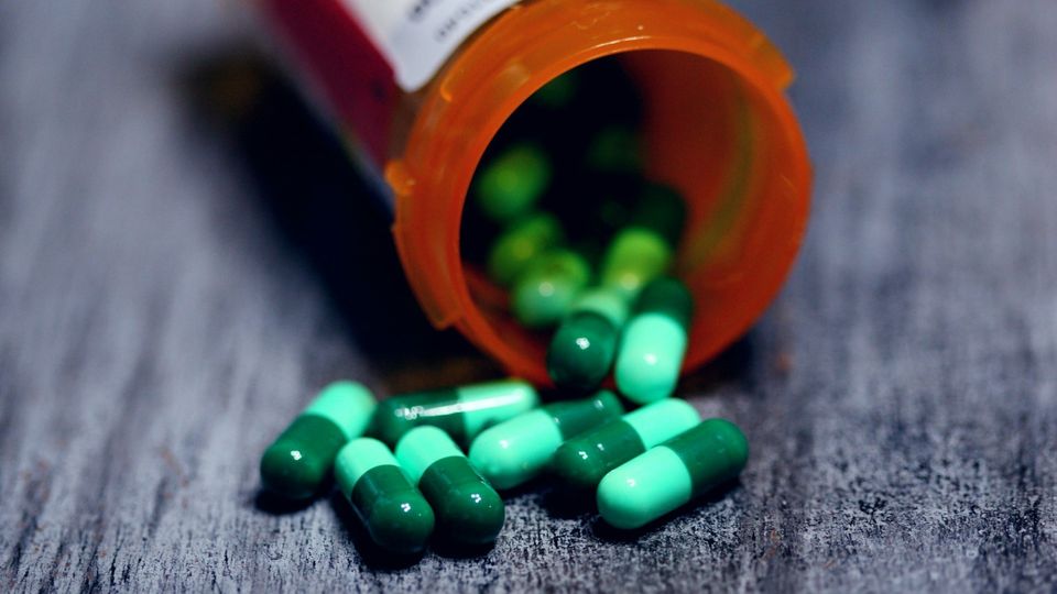 Open prescription pill bottle with green capsules spilled onto a wooden surface.