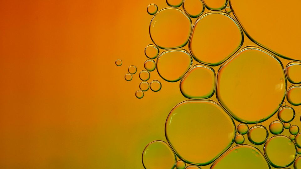 Close-up of colorful liquid bubbles forming an abstract pattern on an orange background.