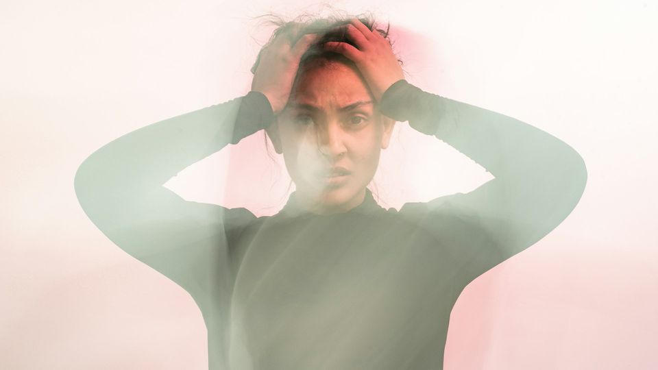 A woman holds her hands to her head, looking in pain.