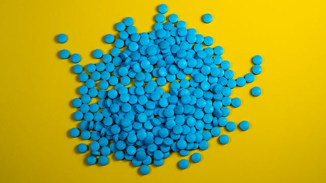 Blue round tablets piled on a bright yellow background, commonly associated with Viagra. 