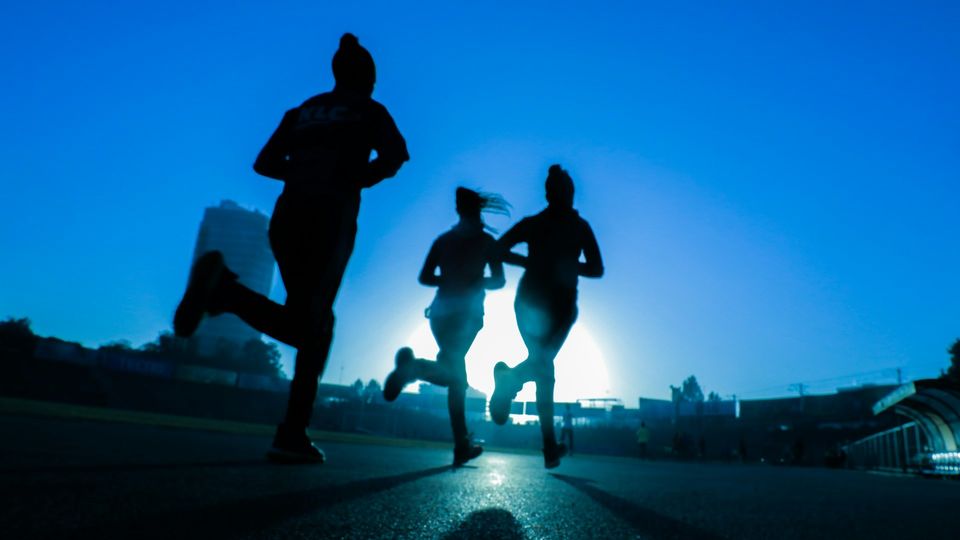 Silhouettes of runners exercising outdoors at sunrise.