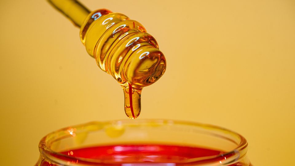 A honey dipper drawing a spoonful of honey out of a glass jar.