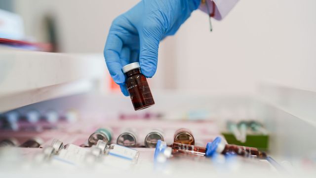 A gloved hand handling a vial of a therapeutic in a laboratory. 