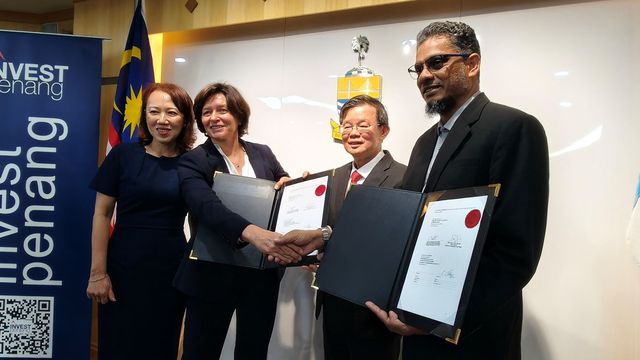 People shaking hands during a partnership signing ceremony while holding signed agreement documents. 