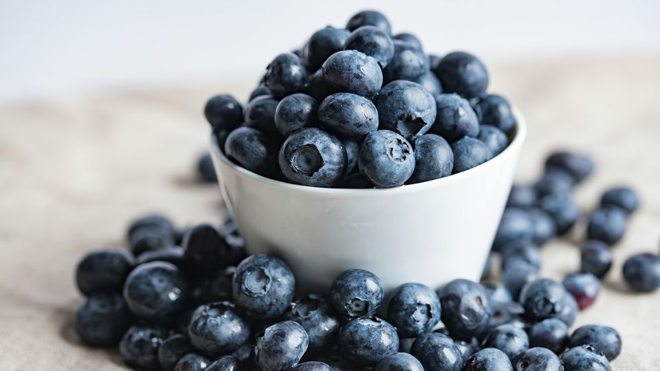 Bowl of fresh blueberries with scattered berries, a natural source of polyphenols.