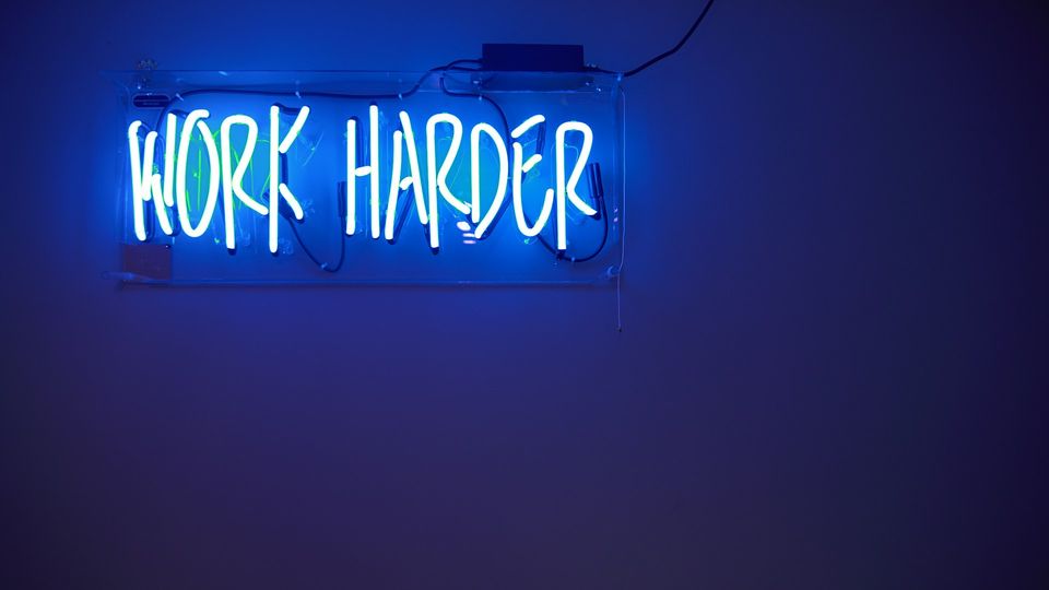 Neon "Work Harder" sign glowing on a dark wall.