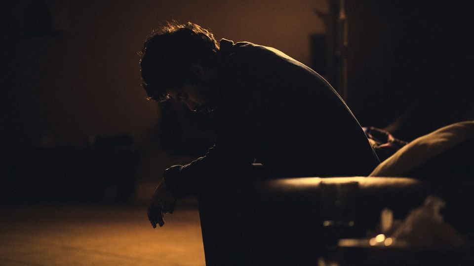 Boy sitting alone in dim light with his head bowed.