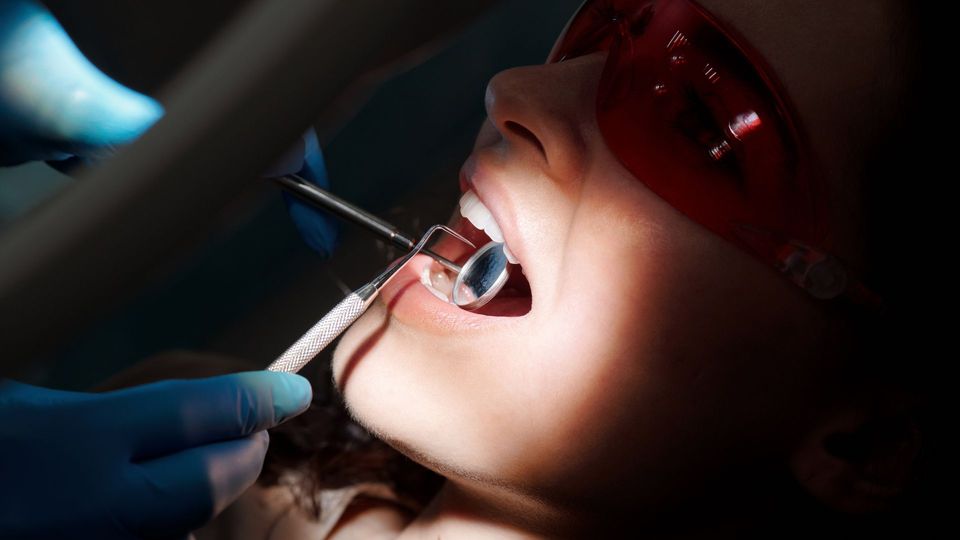 Patient wearing protective glasses during a dental examination with a mirror and dental probe.