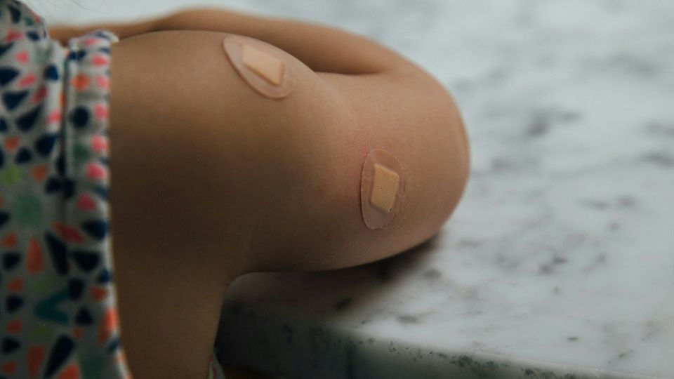 Close-up of a child's upper arm with two adhesive bandages after vaccination.
