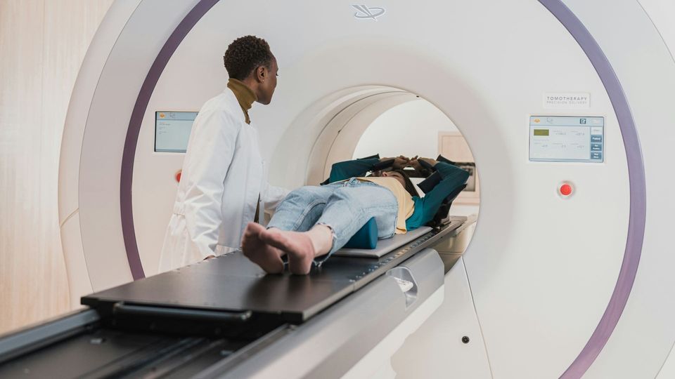 Patient undergoing an MRI scan while a healthcare professional monitors the procedure in the imaging suite.