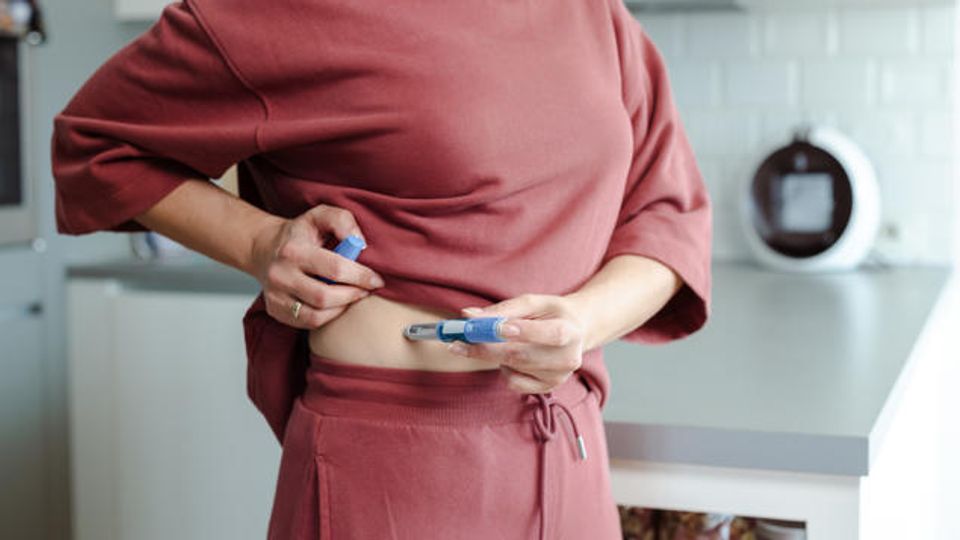 Mid-section of a woman injecting a GLP-1 weight loss treatment into her abdomen.