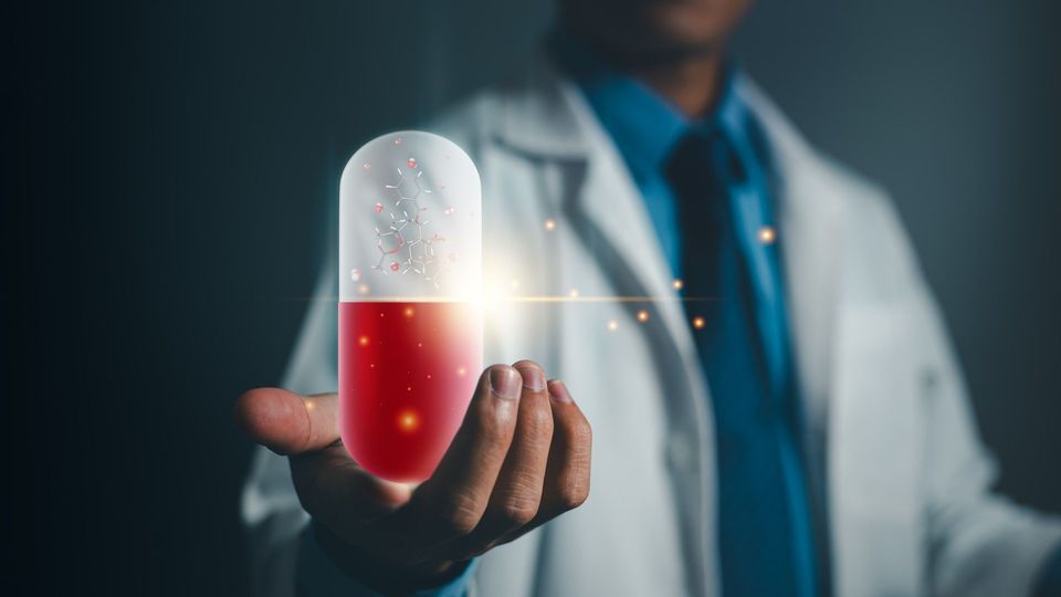 Doctor in a white coat holding an oversized red and white medicinal capsule. The capsule is glowing and contains a ball and stick model. 