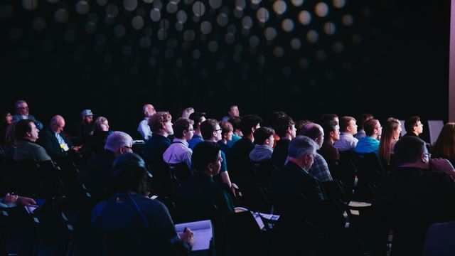 People sitting in rows within a conference room, all looking toward the presentation. 