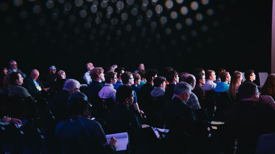 People sitting in rows within a conference room, all looking toward the presentation.