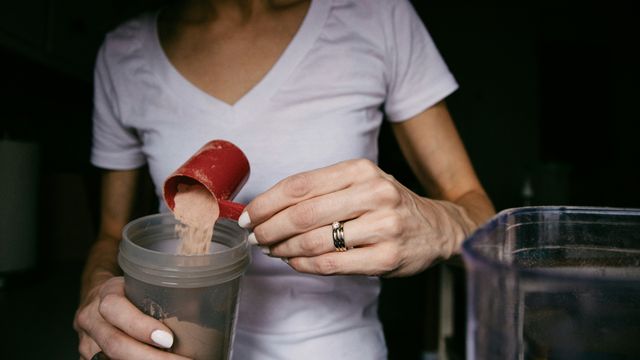 A woman pouring a scoop of protein powder into a shaker bottle. 