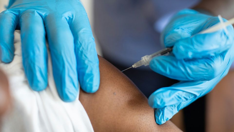 Healthcare worker administering a vaccine injection into a patient's upper arm.