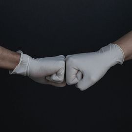 Gloved hands of scientists touching fists in a laboratory teamwork gesture against a dark background. 