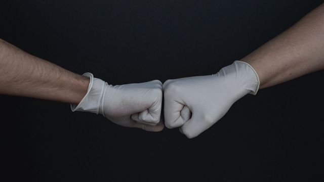 Gloved hands of scientists touching fists in a laboratory teamwork gesture against a dark background. 